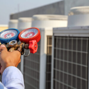 Technician using manifold gauge is measuring equipment for filling industrial factory air conditioners after cleaning and checking for maintenance outdoor air compressor unit.